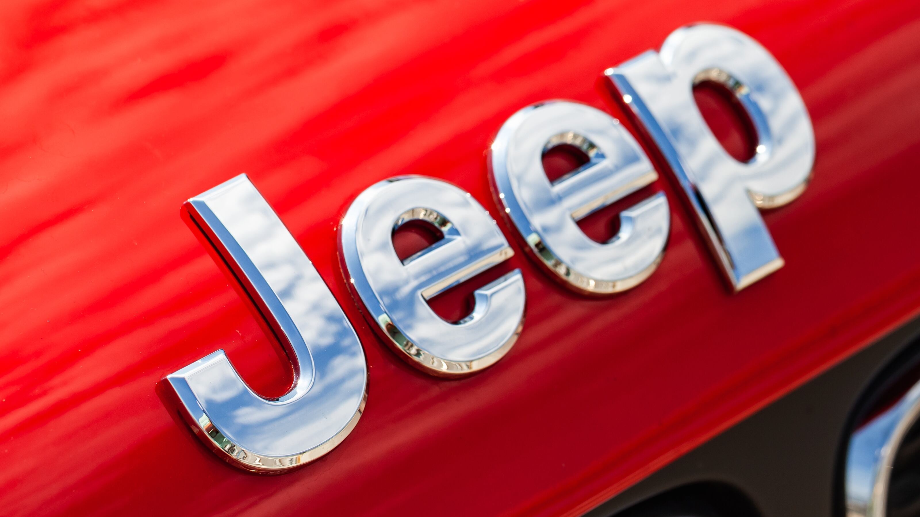 Chromed Jeep car logo mounted at red SUV car hood, macro photo with soft selective focus